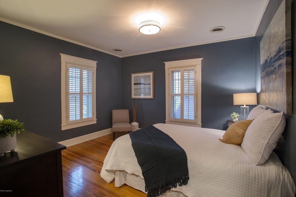 bedroom with furniture, hardwood floors, linavy wall paint, plantation shutters, white comforter, bedside table, bedside lighting, navy throw, art over bed