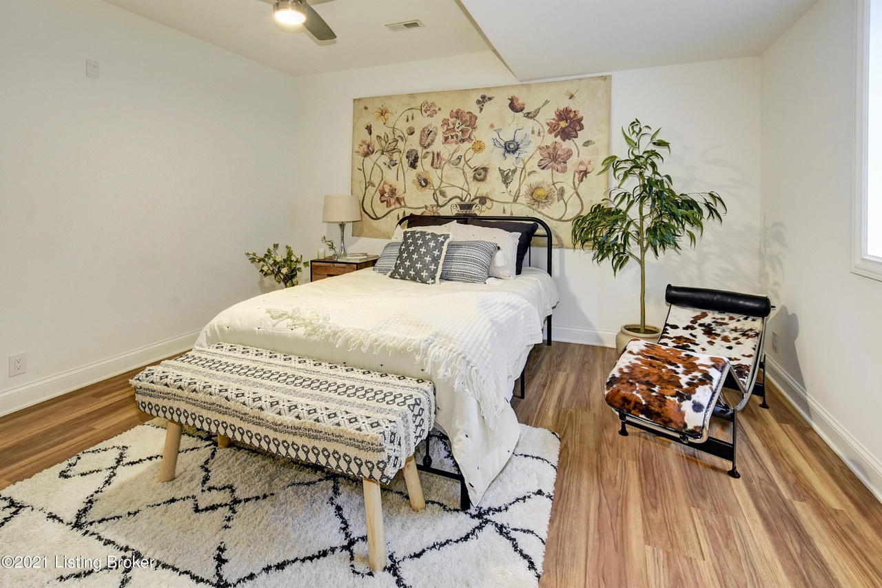 bedroom staging louisville, black and white geometric rug, tribal print bench, large floral artwork, cowhide lounge chair, white bedding, black iron bed, white painted bedroom