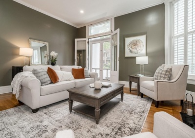 modern living room, sage green paint, white sofa, area rug, medium brown wood tones, honey oak hardwood floors, drum shades,
