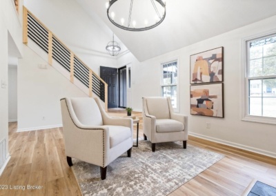 entryway, sitting area, two cream accent chairs, staircase, light wooden floors, modern chandelier